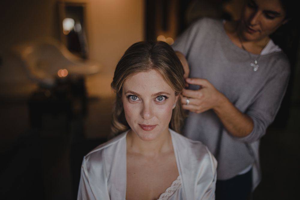 Getting ready scene with someone in a white satin robe during wedding preparations.
