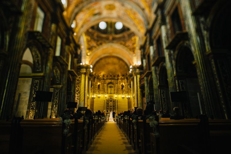 Interior of a grand cathedral with ornate golden ceiling and rows of pews during a wedding ceremony.
