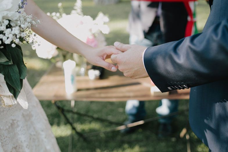 Close-up of hands during ring exchange ceremony at outdoor wedding.