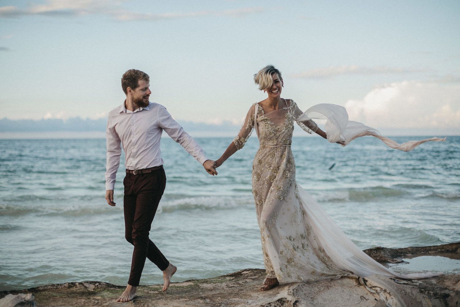 A couple holds hands while walking along a scenic ocean shoreline.