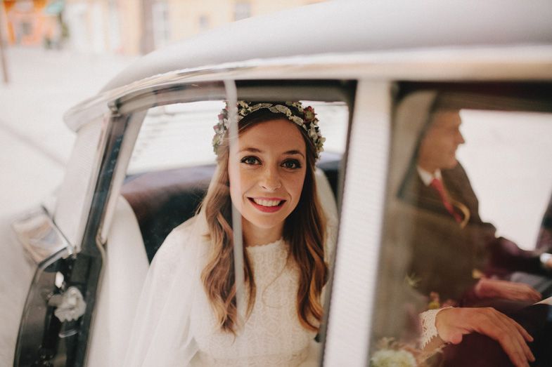 A classic car window frames a happy bride wearing a floral crown and veil.