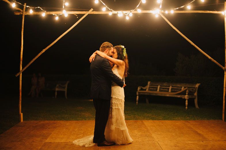 Newlyweds share a romantic dance under string lights at their outdoor reception.