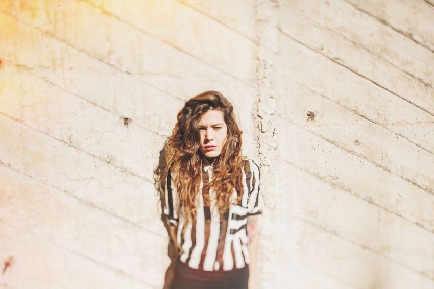 Person in striped shirt poses against textured concrete wall in natural lighting.