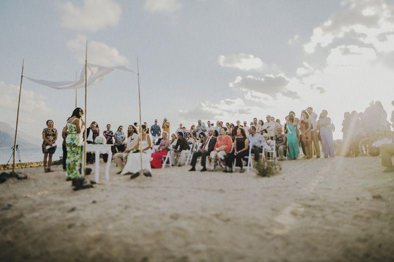 Large outdoor gathering of people seated on a hillside during a sunny event.