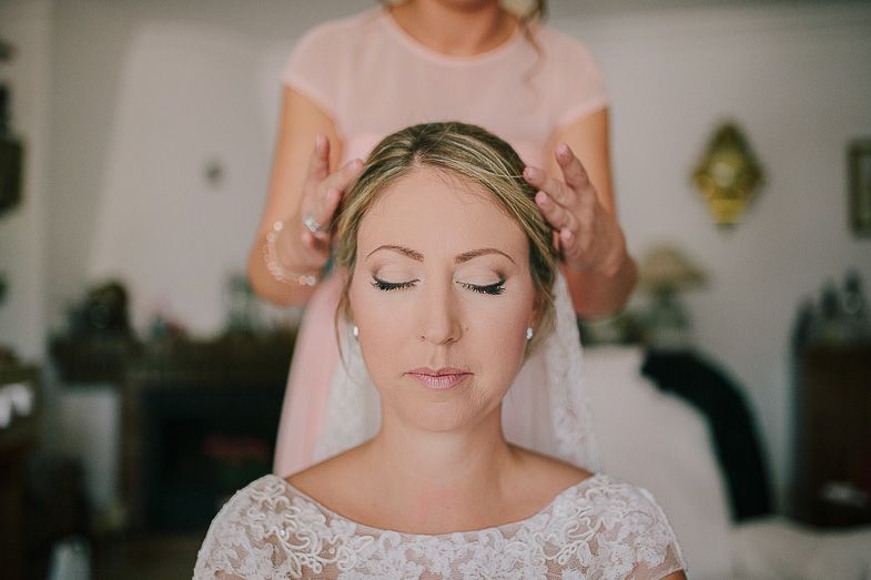 Bride in lace dress with closed eyes and braided crown during wedding preparations.