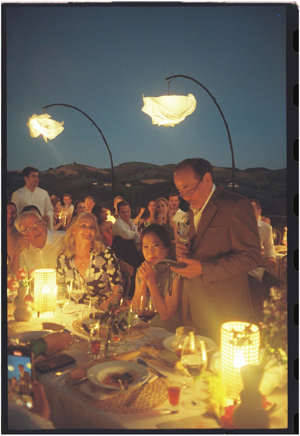 An outdoor evening wedding reception with glowing paper lanterns and candlelit tables.