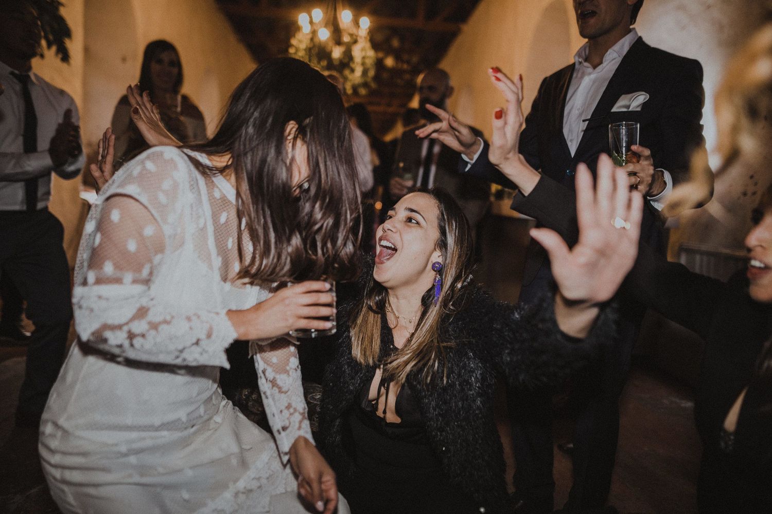 Wedding reception guests dancing and celebrating under chandelier in rustic venue.