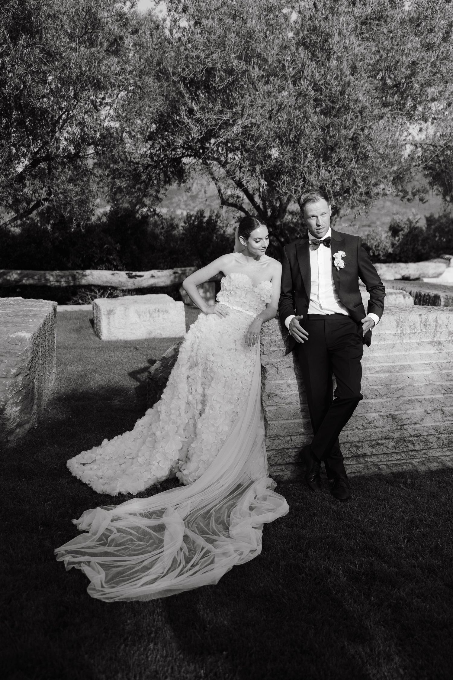 Black and white portrait of newlyweds in formal attire against garden backdrop.