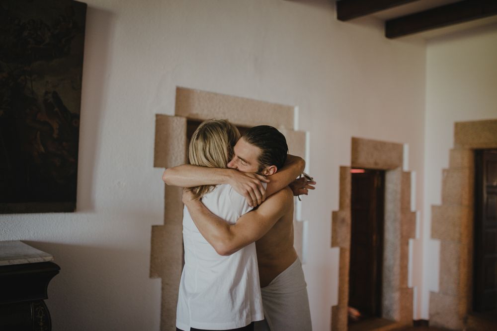 Two people embrace in bright room with stone walls and doorways.