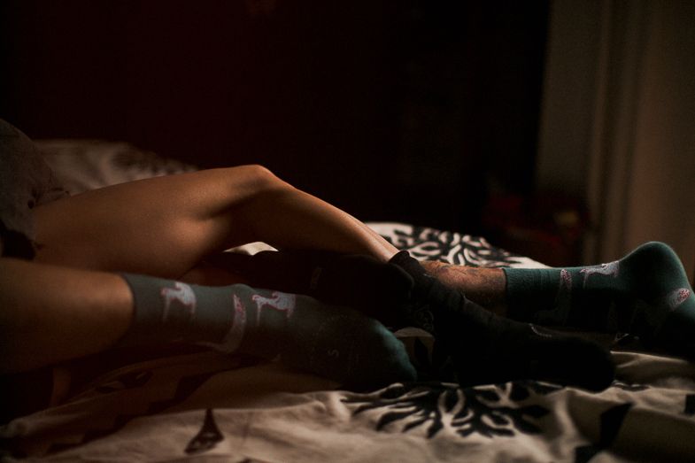 Moody boudoir photograph showing legs with socks on patterned bedding in dim lighting.
