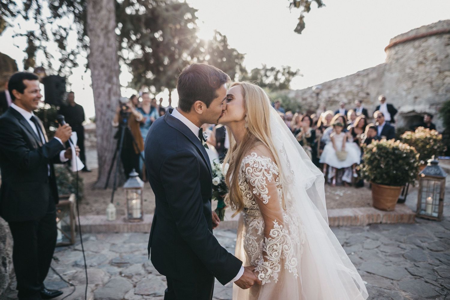 Newlyweds sharing their first kiss at an outdoor wedding ceremony surrounded by guests.