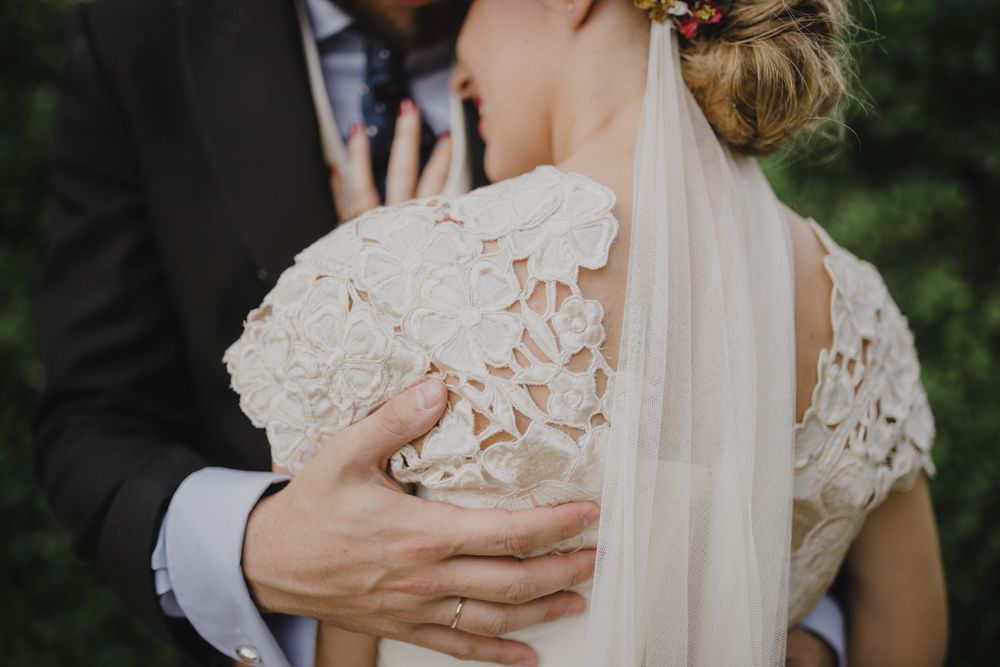 Close-up detail of lace wedding dress and gentle embrace.
