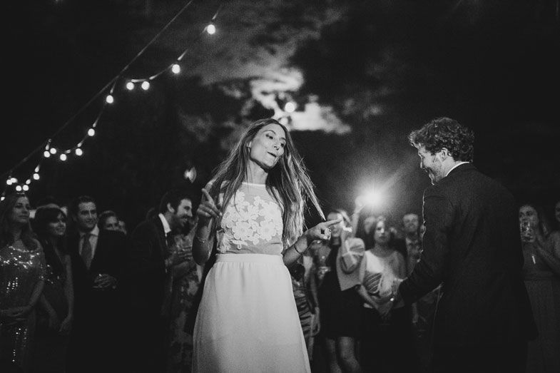 A couple dances under string lights during their outdoor evening wedding celebration.