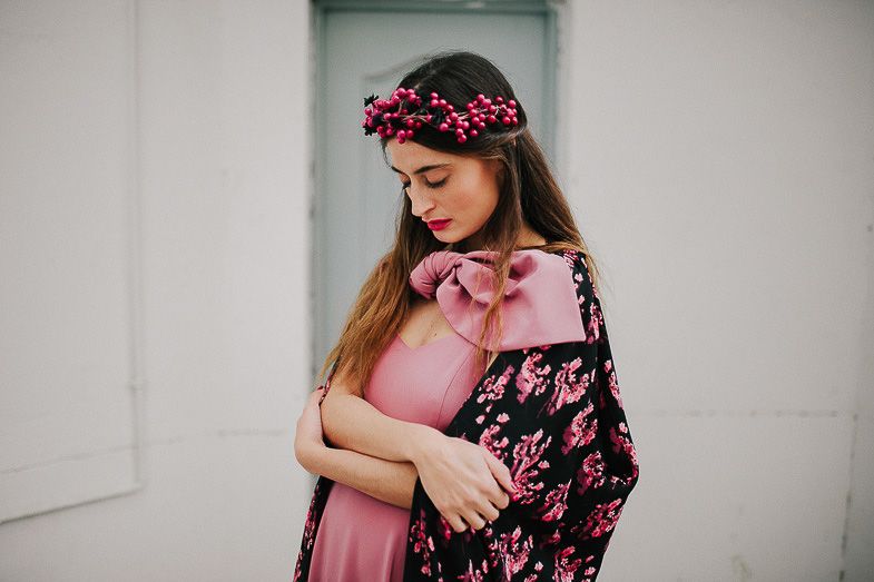 Woman in pink dress and floral crown poses against white wall with matching floral kimono.