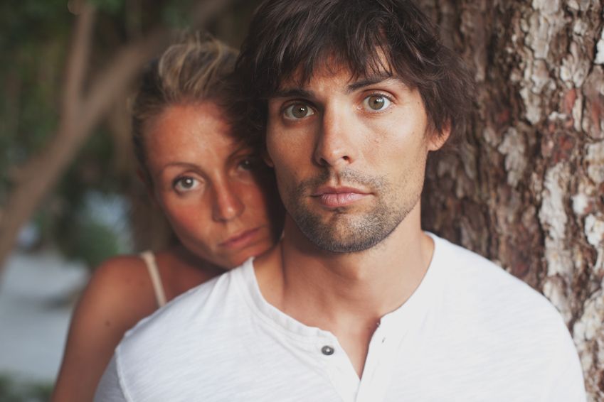 Intimate portrait of couple posing against tree trunk in natural setting.