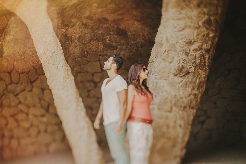 Two people stand between stone archways in a rustic Mediterranean setting.