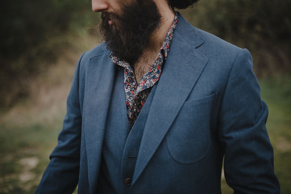 Close-up of a blue suit jacket with patterned shirt and full beard.