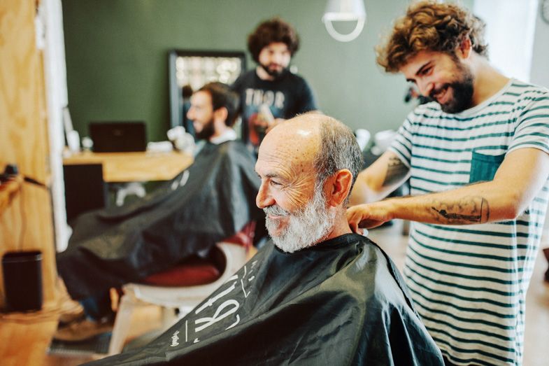 Professional barber giving a haircut to an elderly client with white beard in a modern barbershop.