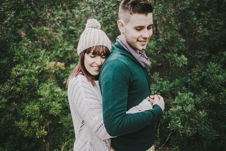 A couple poses playfully in outdoor setting with green foliage background.