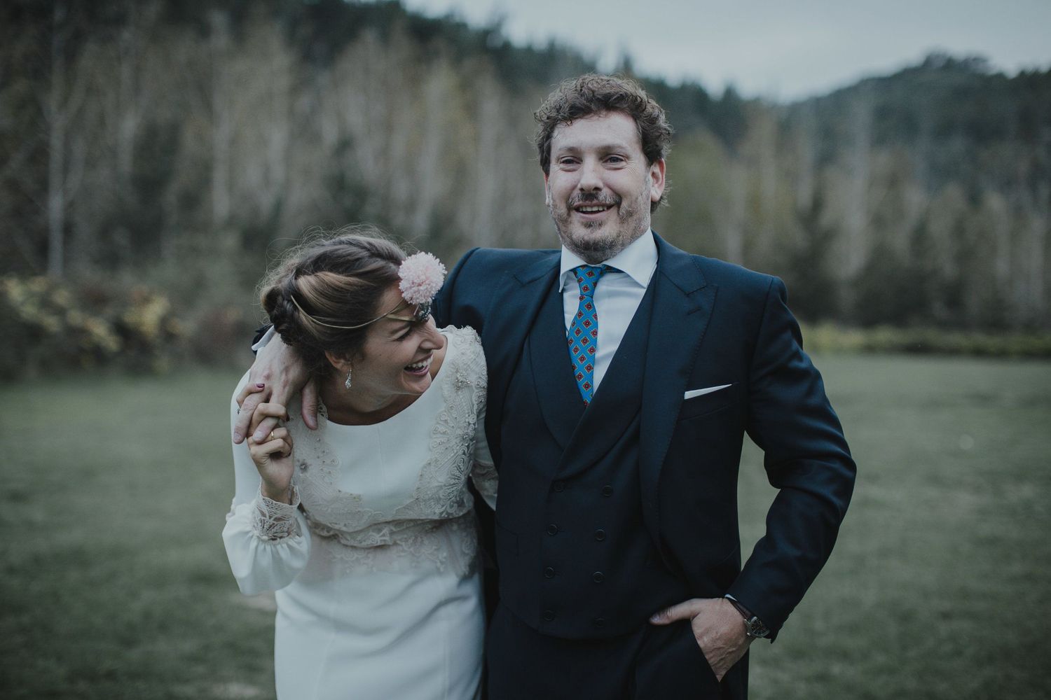 A joyful outdoor wedding portrait featuring a couple in traditional wedding attire against a rural landscape.