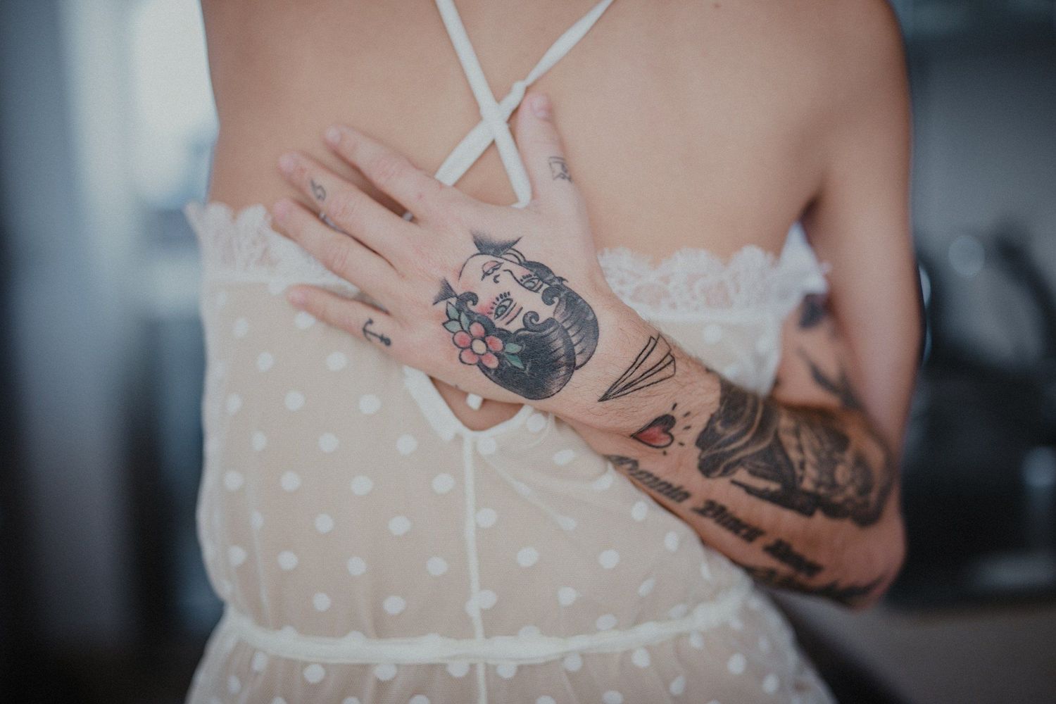 Close-up of tattooed arms embracing around waist in polka dot dress.