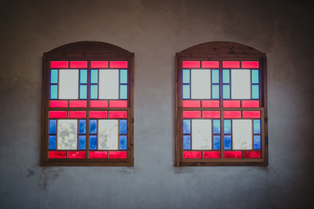 Two identical red and blue stained glass windows on a beige wall with arched tops.
