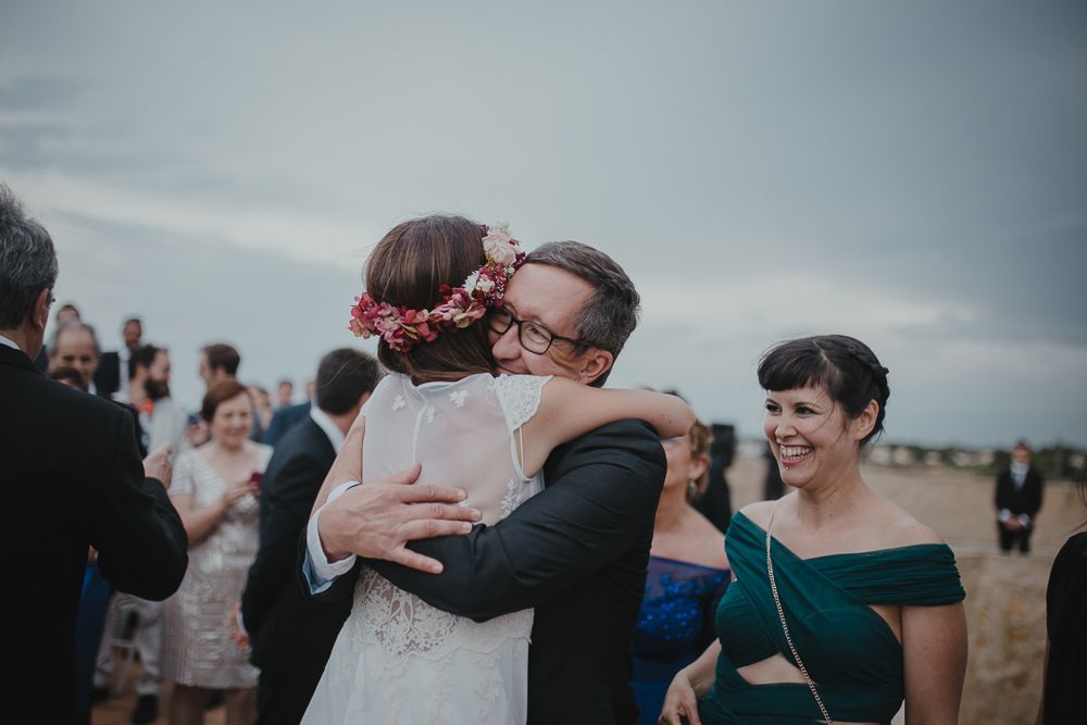 Guests celebrate during an emotional wedding reception outdoors under cloudy skies.