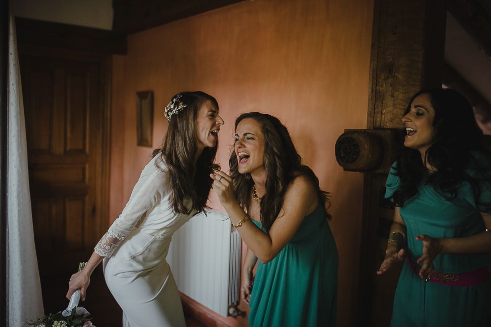 Candid moment of laughter between wedding party members in white and teal dresses.