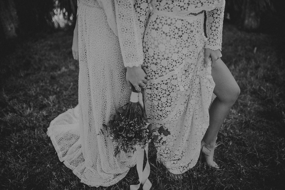 Black and white image of two people wearing vintage-style lace dresses holding bouquets.