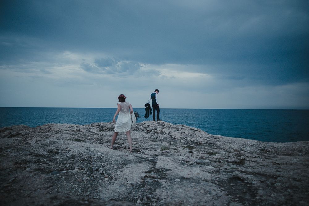 Three silhouettes stand on a rocky coastal overlook during a wedding shoot.