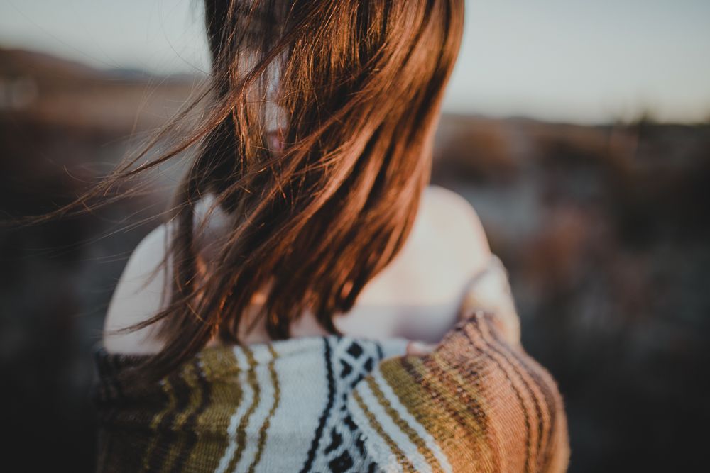 Close-up of long hair blowing in the wind against a sunset backdrop wearing a patterned sweater.