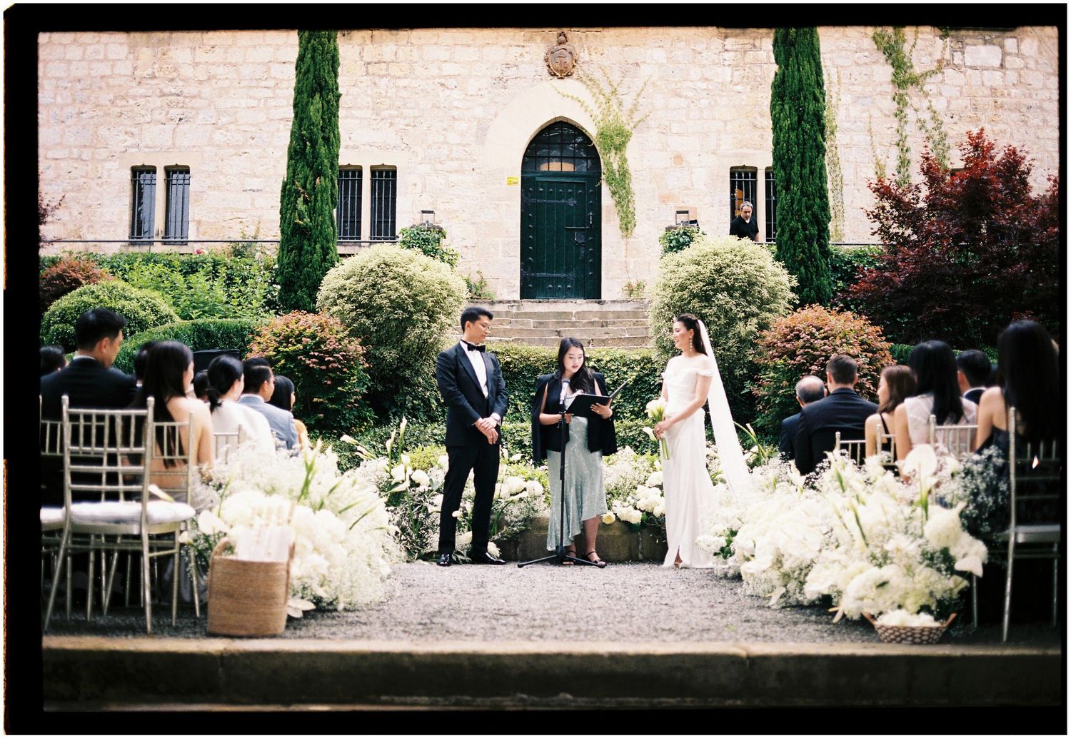 A panoramic collage of wedding scenes at an elegant stone venue with cypress trees and white floral decorations.