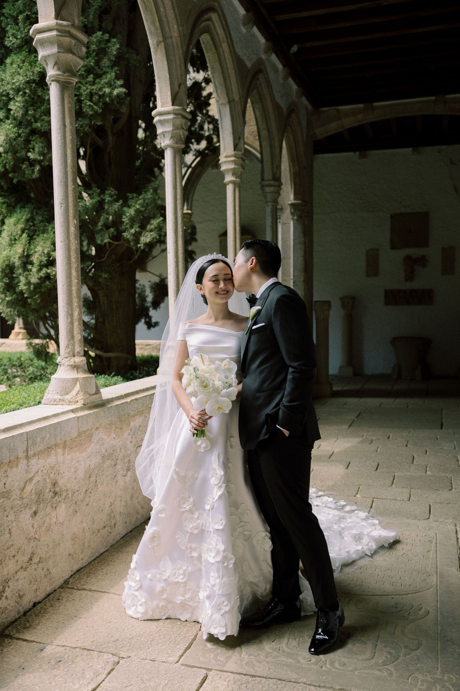 A romantic wedding photoshoot under a columned archway with classic architecture.