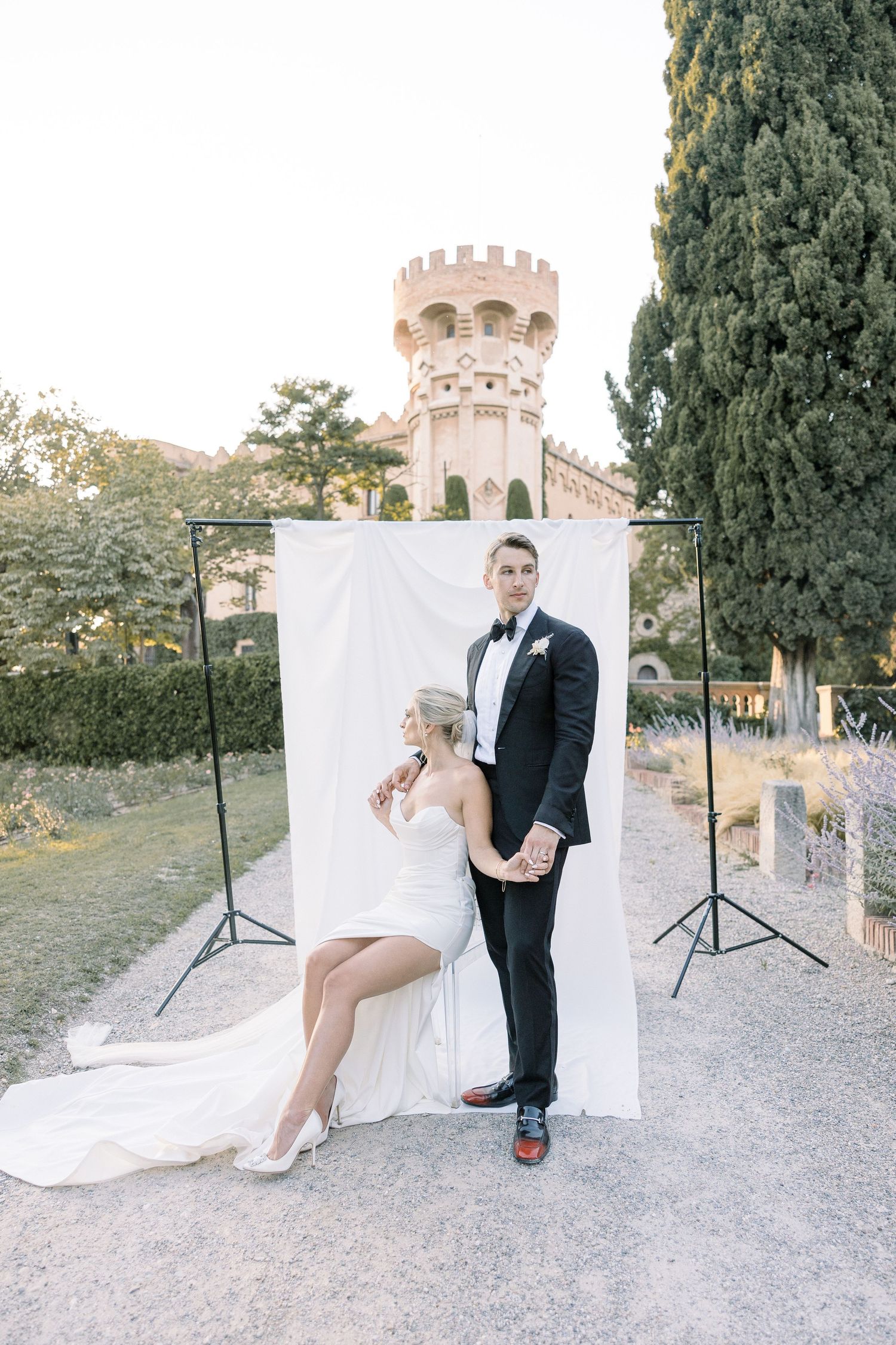 Elegant wedding photoshoot against a stone castle tower backdrop with white fabric backdrop setup.