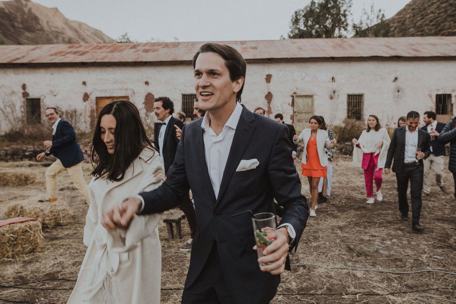 Elegantly dressed couple walking outside historic white building during celebration.
