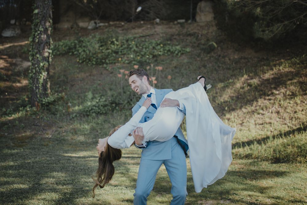 Playful wedding portrait with dramatic dip pose in outdoor woodland setting.