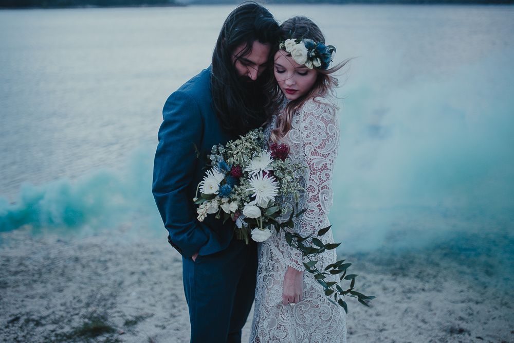Intimate wedding moment captured with teal smoke and white bouquet by the water.