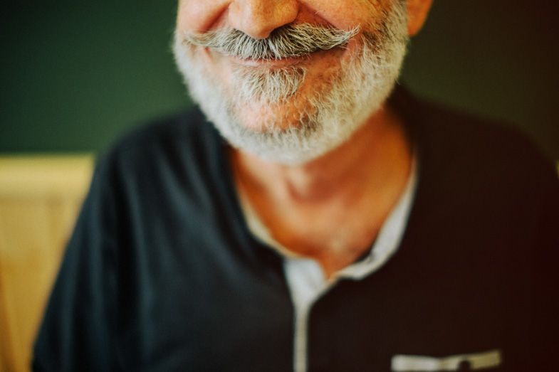 Close-up shot of grey facial hair and closed eyes against a dark background.