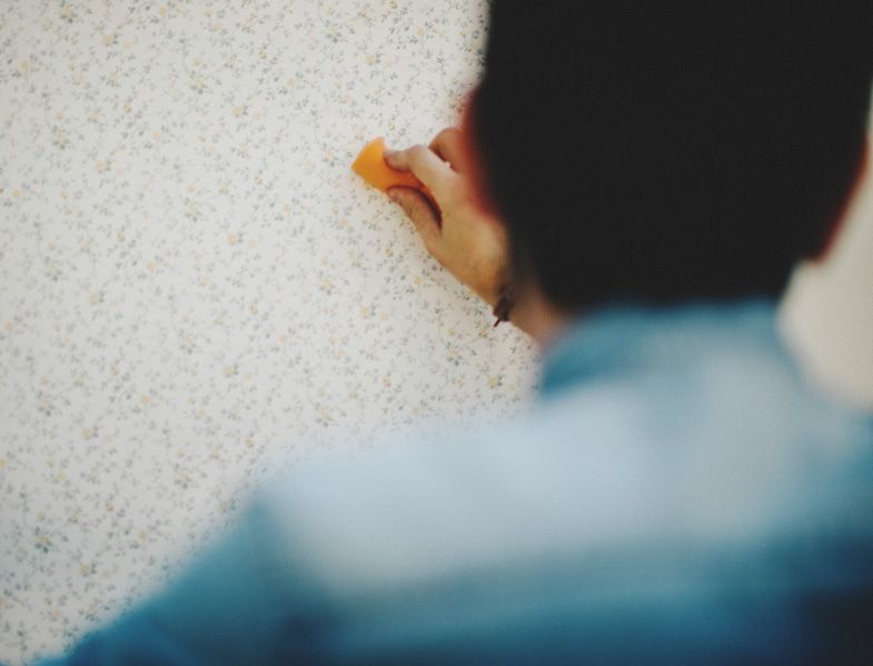 Person removing old wallpaper from wall in close-up shot.