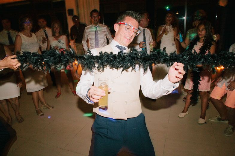 A guest wearing a white shirt dances enthusiastically with a garland at a wedding reception celebration.
