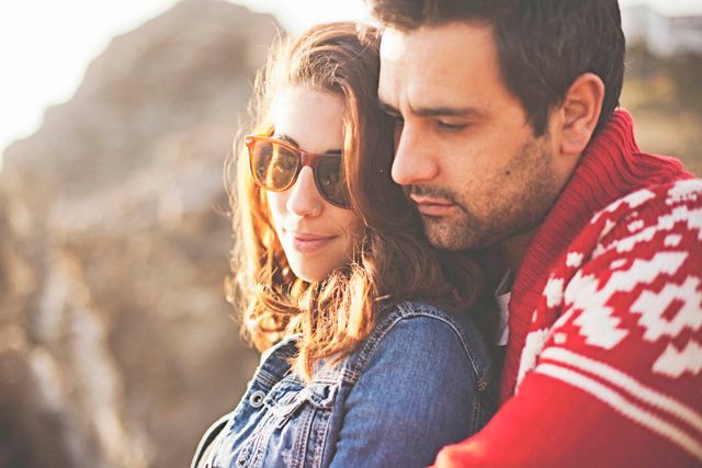 Stylish couple in denim and red sweater pose together in sunset lighting.
