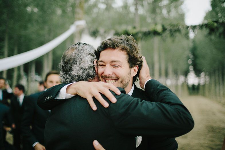 Two people share a warm embrace during an outdoor wedding celebration surrounded by trees.