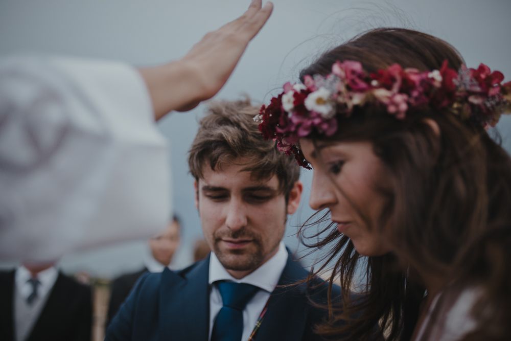 A heartfelt moment during a wedding blessing with a bride in a floral crown outdoors.