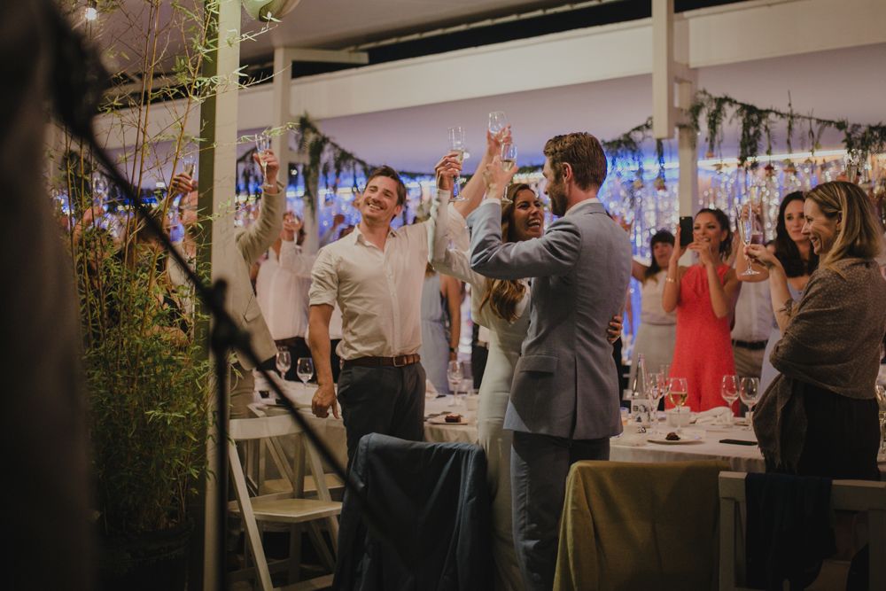 Wedding guests celebrate under a tent decorated with blue lights and festive decor.