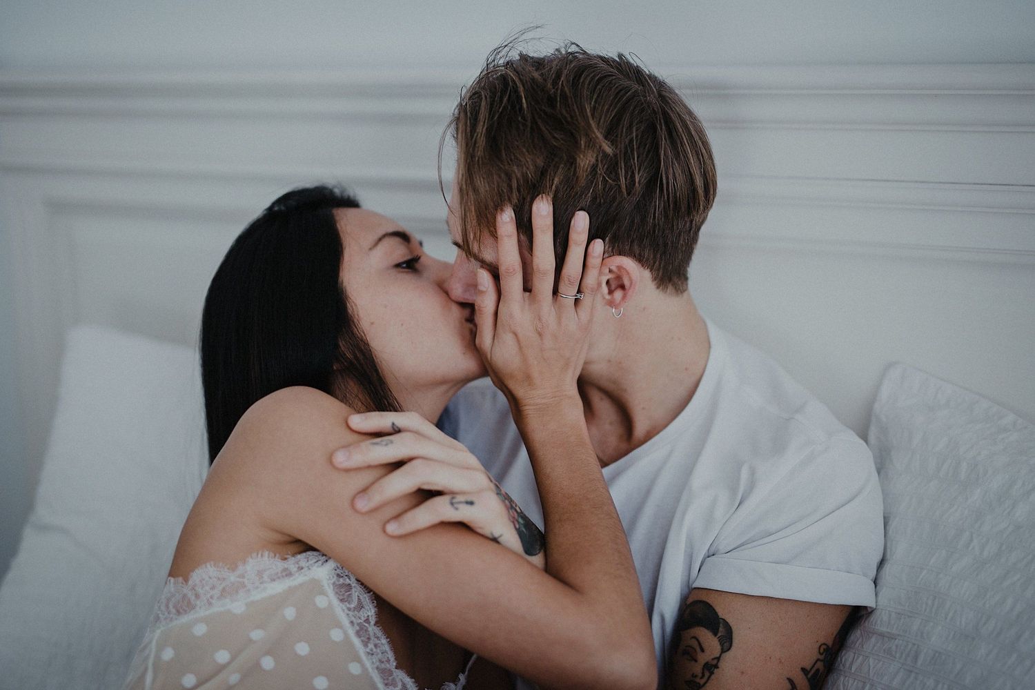 Intimate couple sharing tender kisses in a bright bedroom setting.