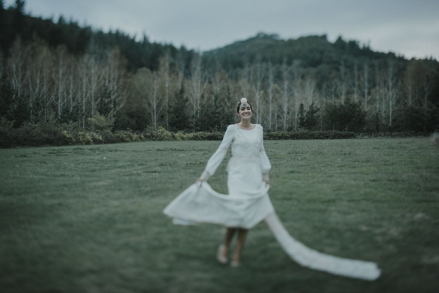 A graceful spin in a white wedding gown with a long train against a moody mountain landscape.