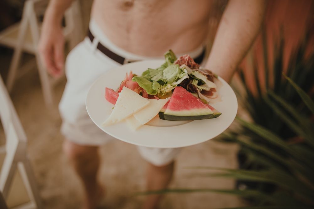 A plate of fresh watermelon and salad greens being held by hands in natural lighting.