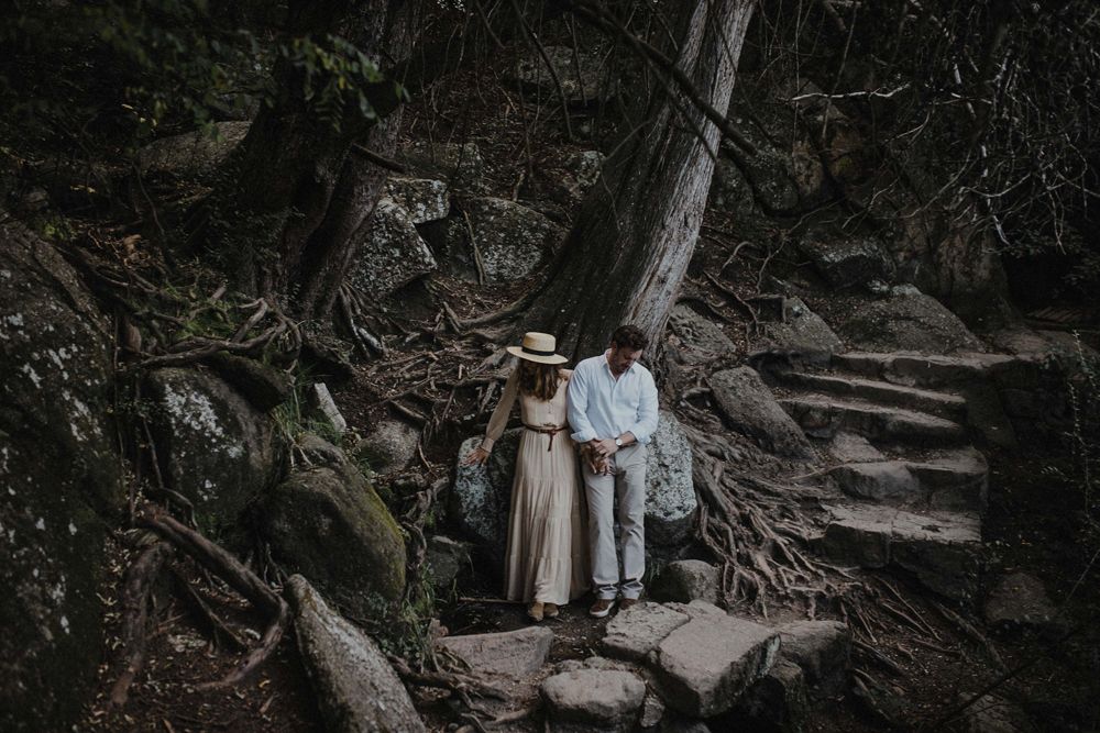 A couple descends stone steps on a rugged forest path.