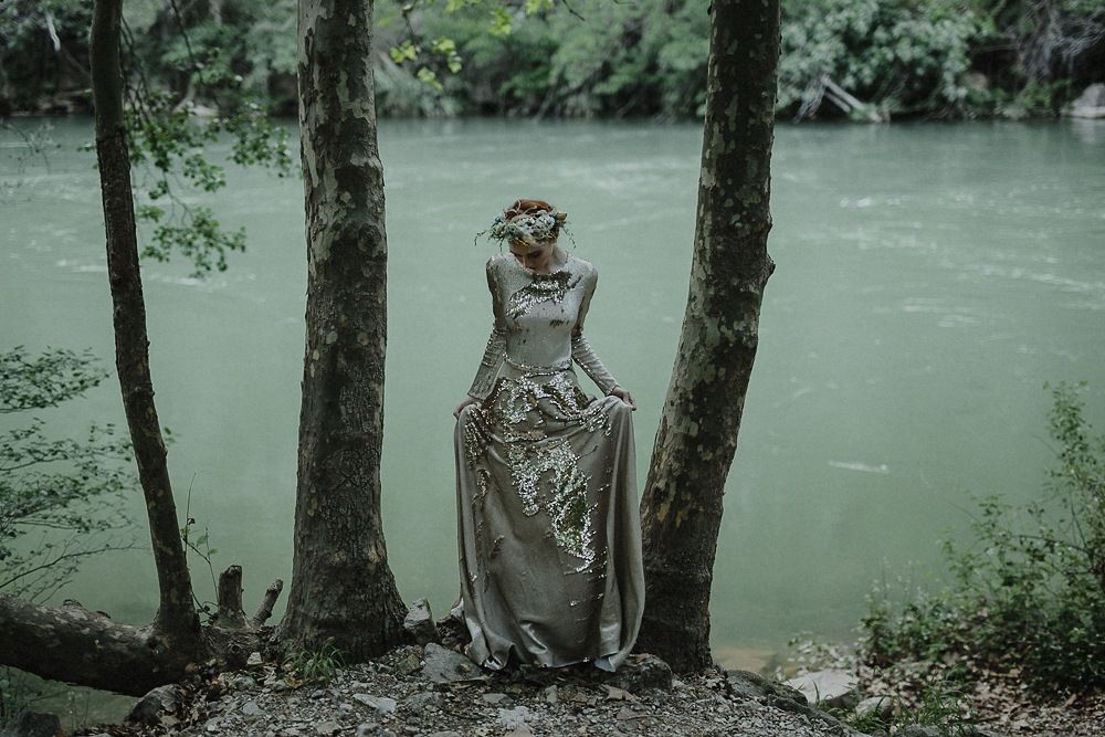 A silver gown catches light among trees beside a misty river.