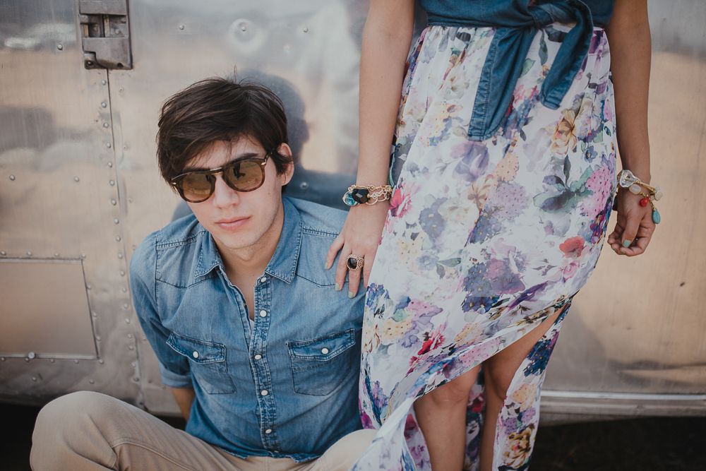 Stylish couple posing against a vintage silver Airstream trailer in the desert.